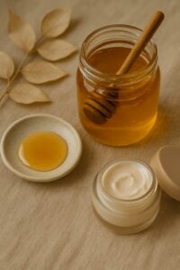 شیشه عسل طبیعی در کنار کرم پوست و ظرف کوچک عسل روی پارچه بژ با نور ملایم طبیعی